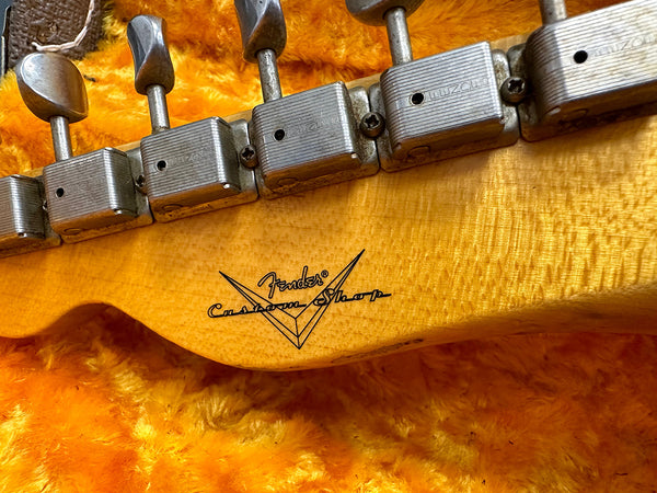Close-up of vintage Fender Custom Shop guitar headstock with metal tuning pegs and natural wood finish on a bright yellow textured background