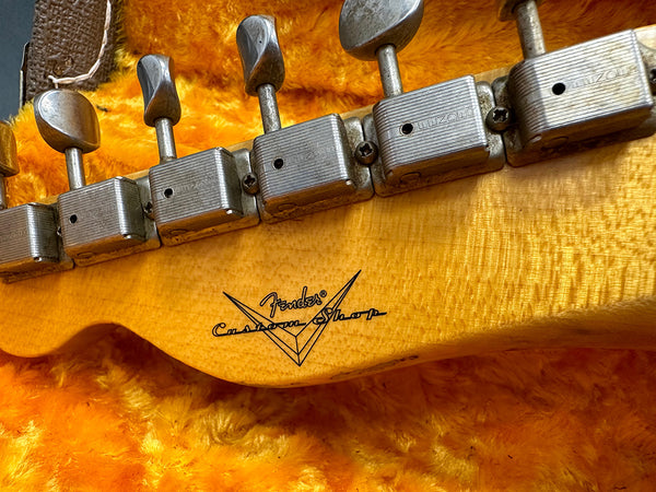 Close-up of vintage Fender Custom Shop guitar headstock with tuning pegs and logo on figured maple wood background in plush yellow case lining.