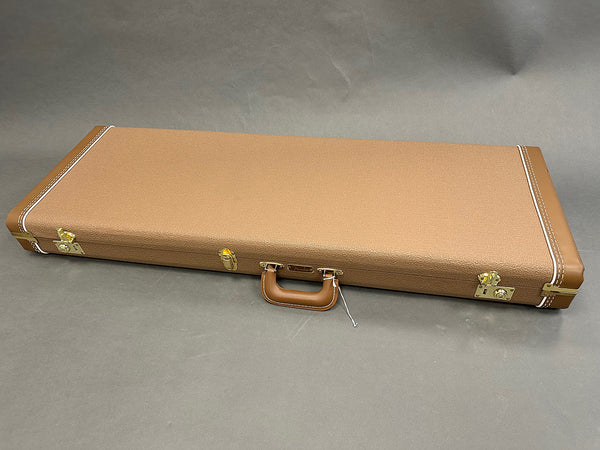 Closed brown textured hard guitar case with leather handle and gold hardware locks on gray background
