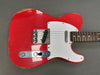 Close-up of red vintage Fender Telecaster electric guitar body with white pickguard, metal bridge plate, and rosewood fretboard, showing wear and aging.