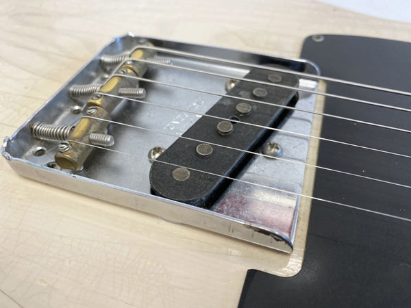 Close-up of vintage Telecaster style guitar bridge with chrome saddles and single-coil pickup on cream-colored body with black pickguard