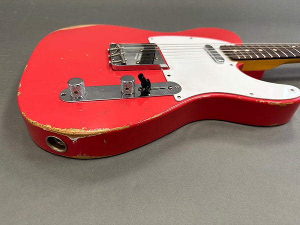 Close-up of vintage red electric guitar body with white pickguard, chrome control knobs, and visible wear on edges, displayed on gray background