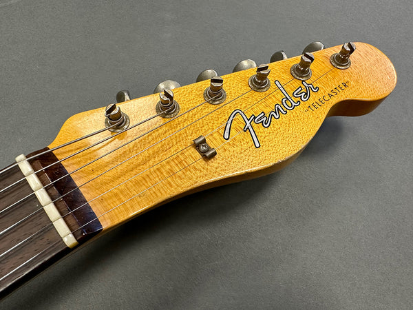 Close-up of Fender Telecaster headstock with six tuning pegs and maple wood finish on gray background