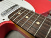 Close-up of red electric guitar fretboard showing rosewood fingerboard with dot inlays and metal frets, part of white pickguard and pickup visible.