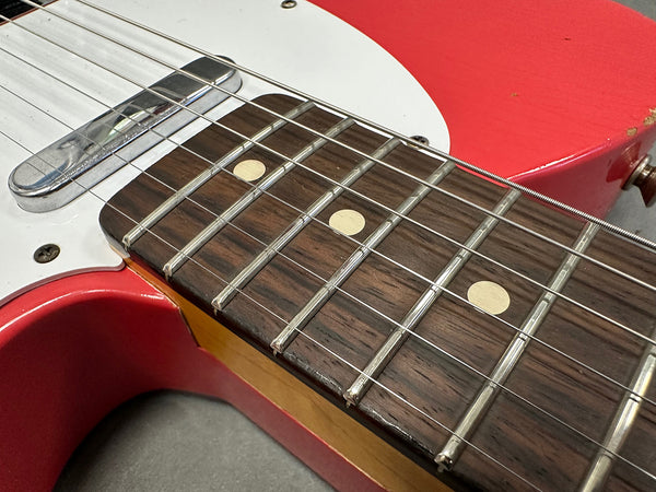 Close-up of red electric guitar fretboard showing rosewood fingerboard with dot inlays and metal frets, part of white pickguard and pickup visible.