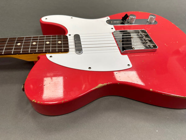 Close-up of red electric guitar body with white pickguard, showing wear and scratches on the finish, featuring chrome hardware and two control knobs