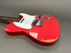 Red electric guitar with white pickguard and two knobs on gray background showing wear and tear