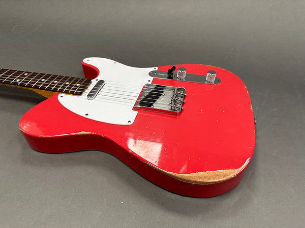 Red electric guitar with white pickguard and two knobs on gray background showing wear and tear