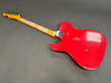 Vintage red electric guitar with worn finish and natural wood neck lying face down on gray surface.