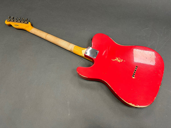 Vintage red electric guitar with worn finish and natural wood neck lying face down on gray surface.