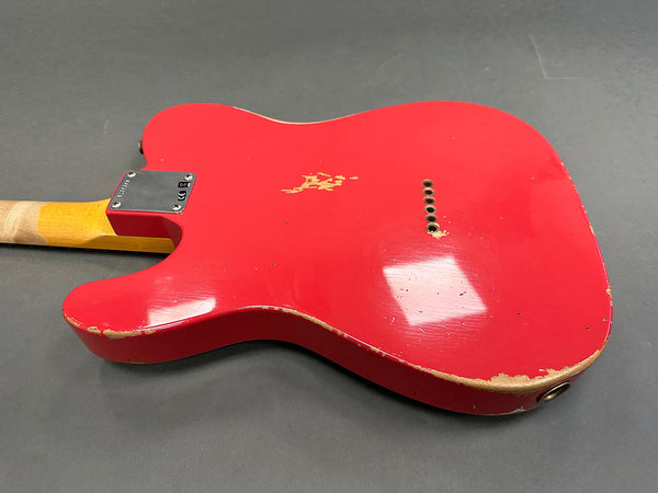 Rear view of red electric guitar body with visible wear and paint chips, showing string ferrules and neck joint on gray background