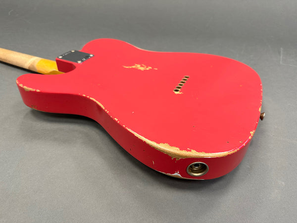 Red electric guitar body with visible wear and paint chips, showing distressed vintage finish and metal input jack on gray background