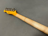 Back view of electric guitar neck with tuning pegs and natural wood finish on gray background
