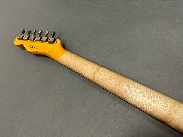 Back view of electric guitar neck with tuning pegs and natural wood finish on gray background