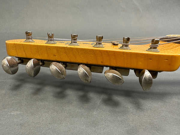 Close-up image of vintage guitar headstock with six metal tuning pegs and wrapped strings on light wood finish