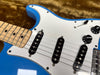 Close-up of blue electric guitar body with white pickguard, maple neck, three single-coil pickups, and black tone and volume control knobs