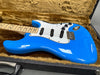 Electric blue solid body electric guitar with white pickguard and maple neck in a plush brown guitar case