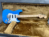 Fender Stratocaster electric guitar in blue with maple neck and white pickguard inside vintage-style hard case with plush brown interior lining.