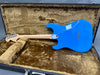 Electric guitar with vibrant blue finish and natural wood neck inside fur-lined hard case viewed from back