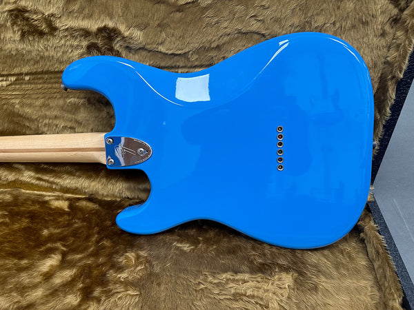 Back view of bright blue electric guitar body with natural wood neck resting in brown fur-lined guitar case