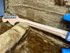Maple neck and chrome tuning pegs on electric guitar with blue body resting in tan plush guitar case interior