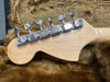 Close-up of maple guitar headstock with six chrome tuning pegs resting on brown plush guitar case lining