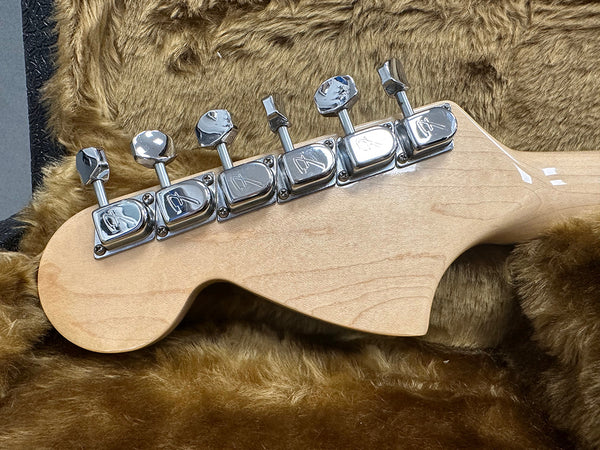 Close-up of maple guitar headstock with six chrome tuning pegs resting on brown plush guitar case lining