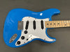 Bright blue electric guitar with white pickguard, three single-coil pickups, maple neck, and chrome hardware on gray background