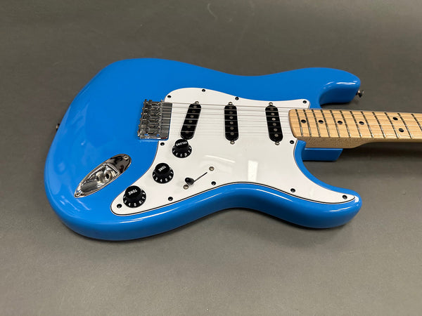 Blue electric guitar with white pickguard, three single-coil pickups, and maple neck on gray background