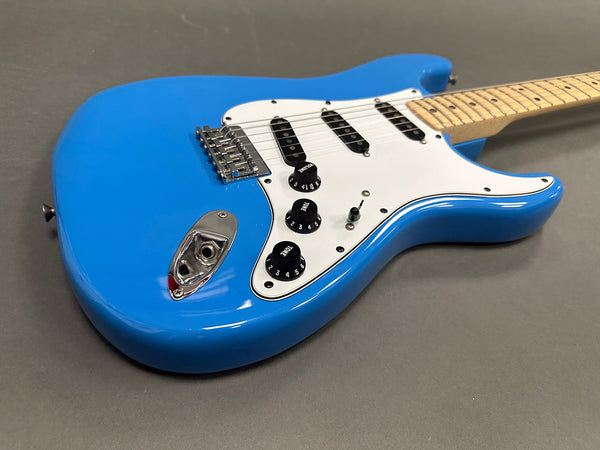 Blue electric solid body guitar with white pickguard, three single-coil pickups, maple neck, and black control knobs on gray background.