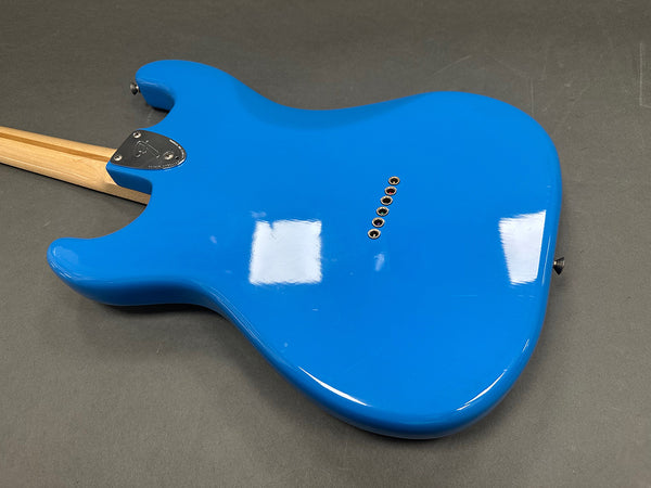 Back view of bright blue electric guitar body with string ferrules and bolt-on maple neck on gray surface