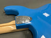 Close-up of blue Fender electric guitar body with silver neck plate and maple neck on gray surface