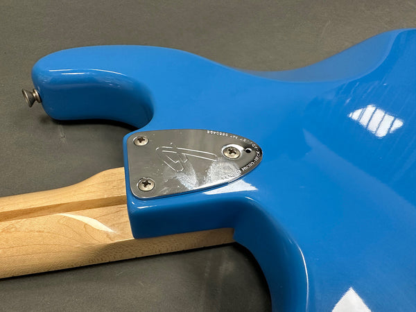 Close-up of blue Fender electric guitar body with silver neck plate and maple neck on gray surface
