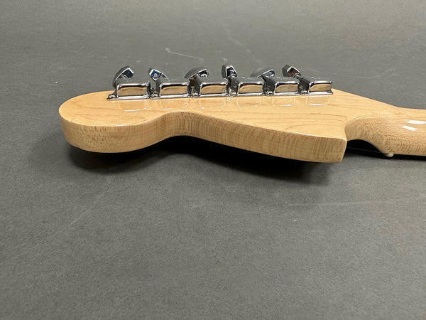 Close-up of guitar headstock with chrome tuning pegs on light wood neck against gray background