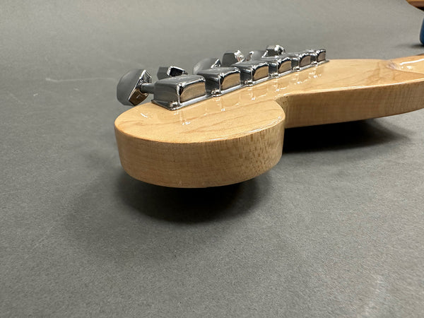 Close-up of natural wood guitar neck headstock with silver tuning pegs on gray background