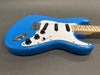 Blue electric guitar with white pickguard, three single-coil pickups, black control knobs, and maple neck on gray background