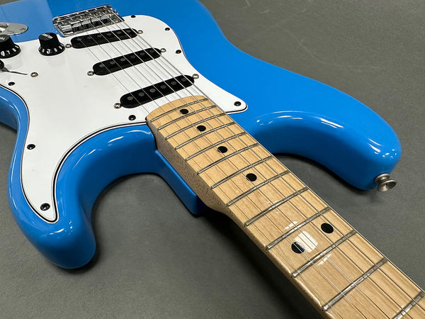 Close-up of blue electric guitar body and maple neck with black dot inlays on grey background