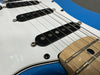 Close-up of blue electric guitar body showing white pickguard, black single-coil pickups, metal strings, and natural wood fretboard.