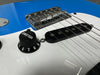 Close-up of electric guitar bridge, single-coil pickup, and black volume knob on white pickguard with blue guitar body background