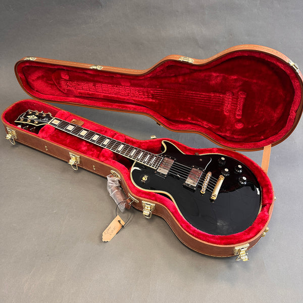 Black electric guitar with gold hardware in open brown hard case with red plush lining on gray background