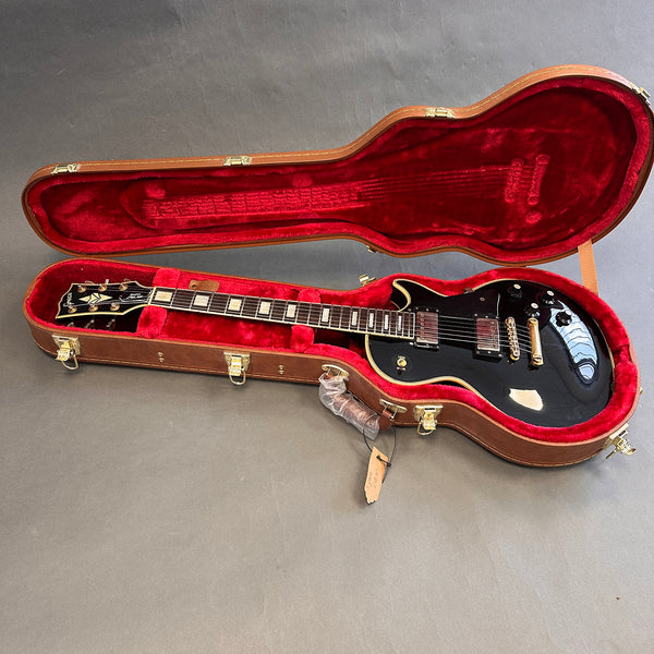 Black Gibson Les Paul electric guitar with gold hardware inside open brown hard shell case lined with red plush interior