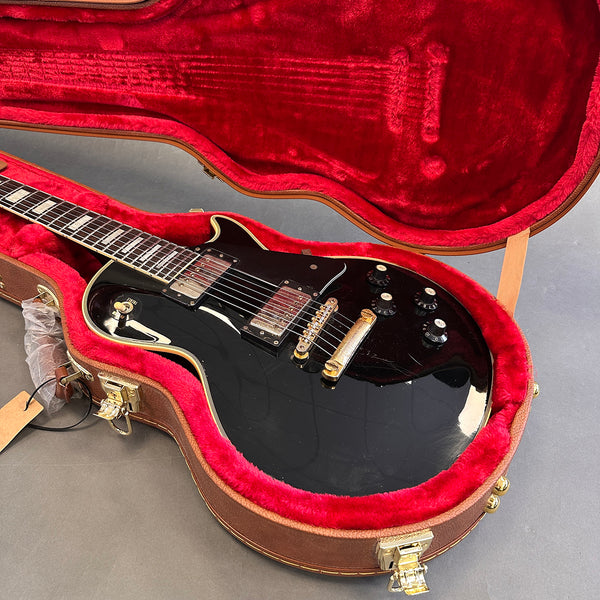 Black electric guitar with gold hardware in red plush-lined brown guitar case on gray surface