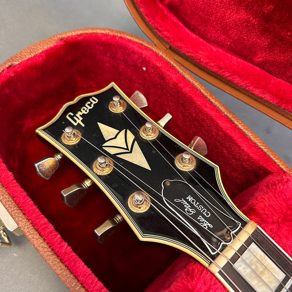 Close-up of Greco Les Paul Custom guitar headstock with vintage tuning pegs inside red velvet-lined brown guitar case