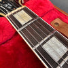 Close-up of Gibson Custom guitar fretboard with mother-of-pearl block inlays, steel strings, and vintage-style binding, displayed in red plush-lined guitar case.