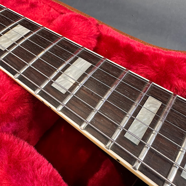 Close-up of electric guitar rosewood fretboard with rectangular pearl inlays and metal frets on red plush case lining