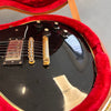 Close-up of black electric guitar with gold bridge and control knobs inside red plush-lined guitar case