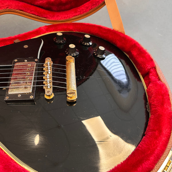 Close-up of black electric guitar with gold bridge and control knobs inside red plush-lined guitar case