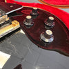 Close-up of black electric guitar control knobs labeled volume and tone with gold hardware and visible scratches on the guitar body inside a red padded case.