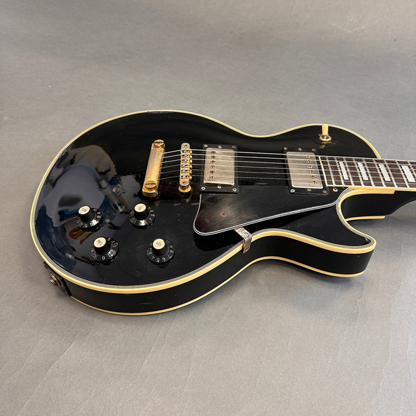 Black electric guitar with cream binding, two humbucker pickups, and four black control knobs on gray background