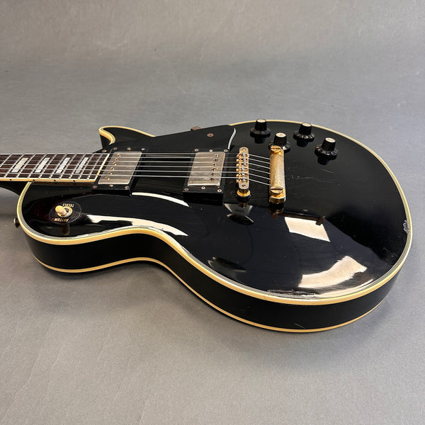 Black electric guitar with dual humbucker pickups, gold hardware, and cream binding showing signs of wear on the body.
